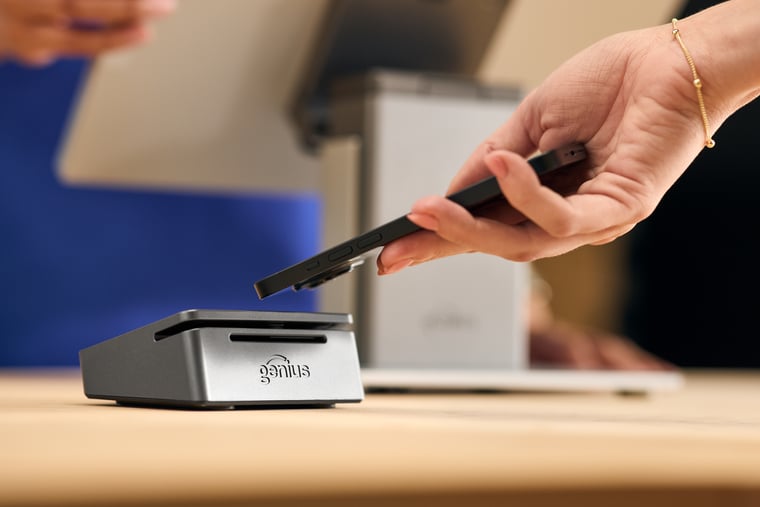 Close-up of hand holding smartphone to tap to pay on point of sale device with server behind counter