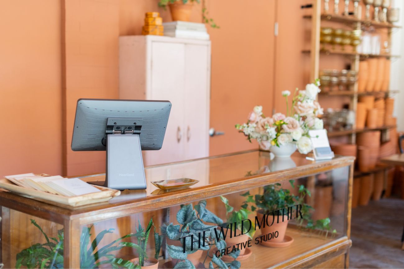 Point of sale terminal sitting on glass counter with flowers and plants inside small business