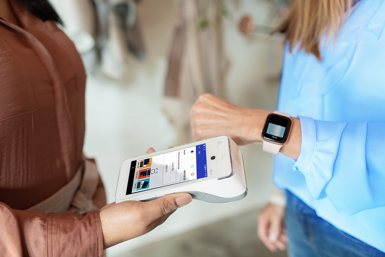 Close-up of person using smartwatch to make contactless payment on handheld point of sale terminal