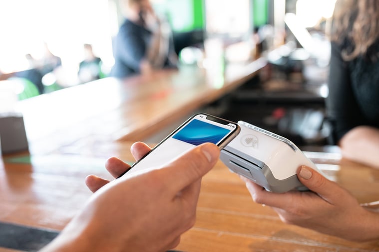 Close-up of hand holding smartphone to make contactless payment on portable point of sale terminal