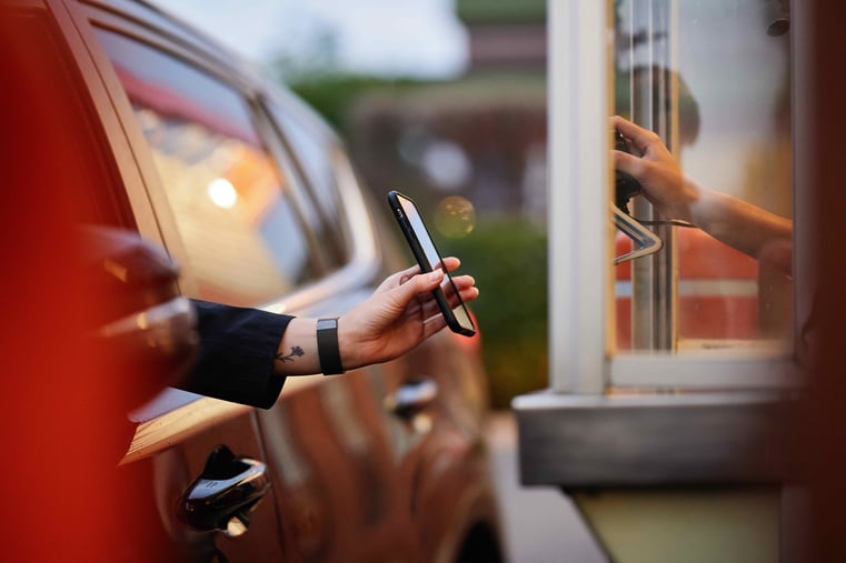 Customer holding smartphone out of car window to make contactless payment at drive-thru
