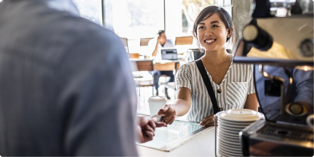 Smiling customer paying barista with credit card at cafe counter