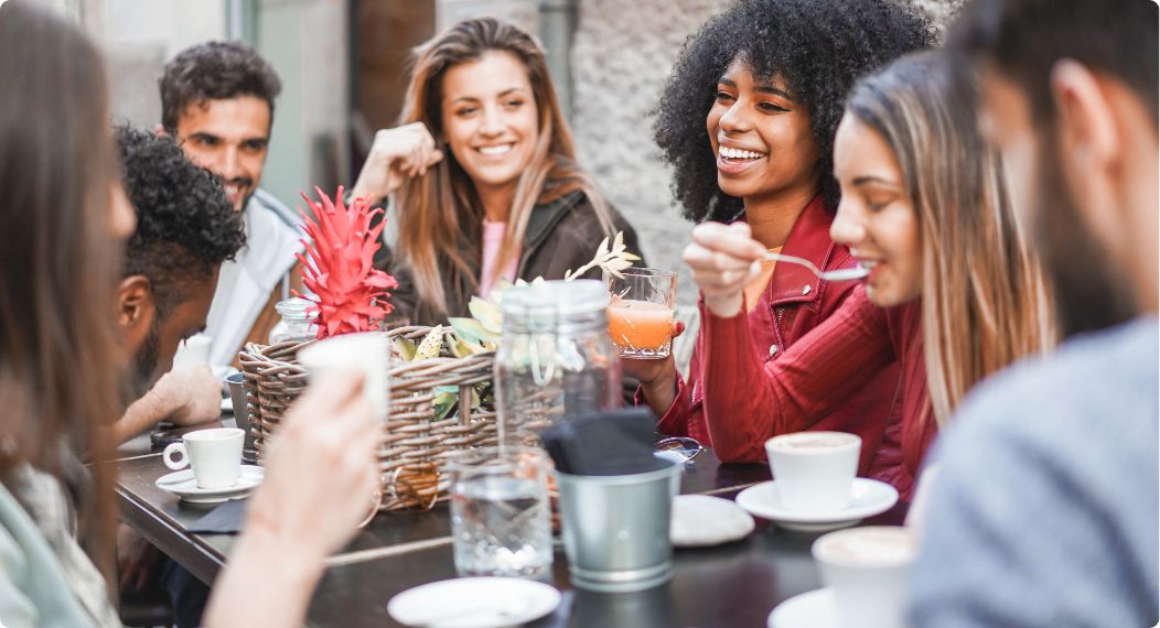 Group of happy friends talking and laughing over coffee and drinks while sitting at outdoor cafe table