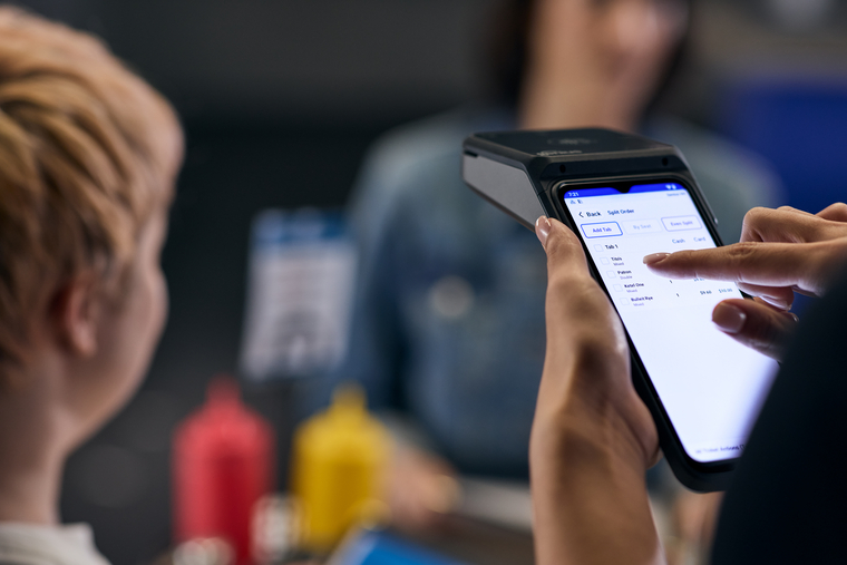 Close-up of server entering customer order on handheld device in bar-and-grill restaurant setting