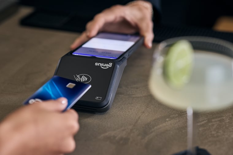 Close-up of customer hand holding credit card while using handheld payment device in bar-and-grill setting