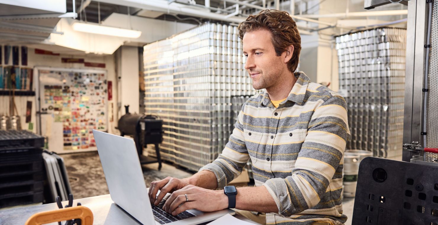A man wearing a striped shirt works at a laptop.
