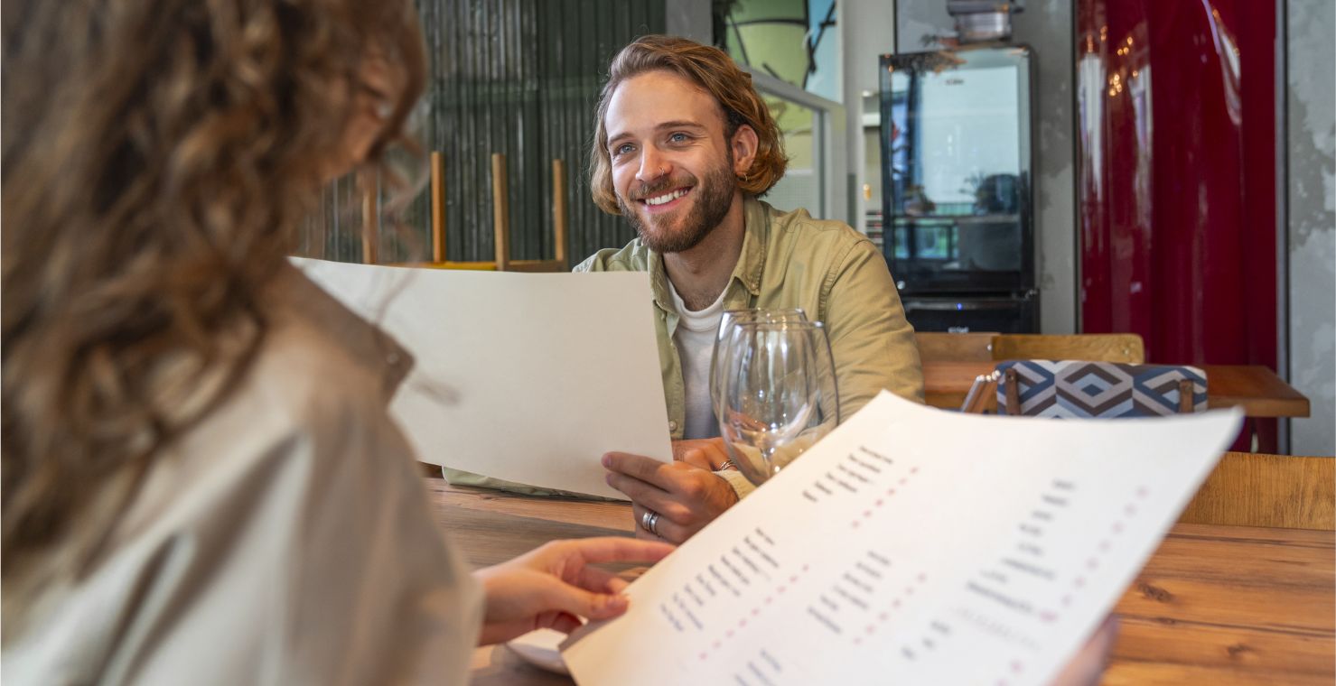 A diner holds a large menu and smiles at another person holding a menu.
