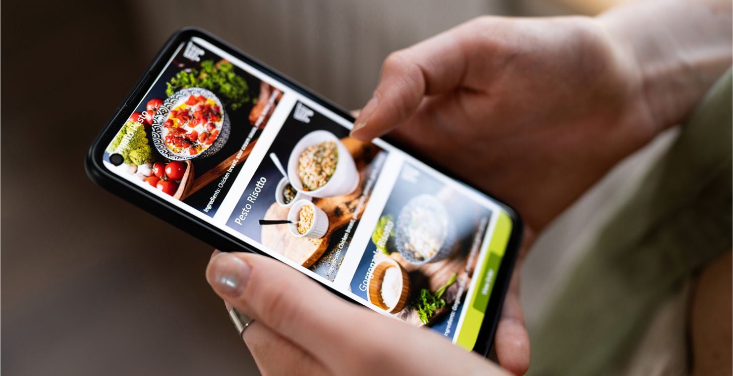 A close-up shot of a phone depicting an online menu with dishes like pesto risotto.