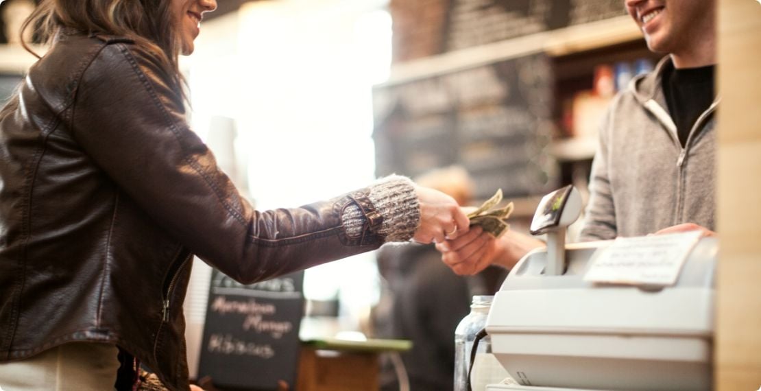 Smiling customer handing cash to cashier near register at store counter