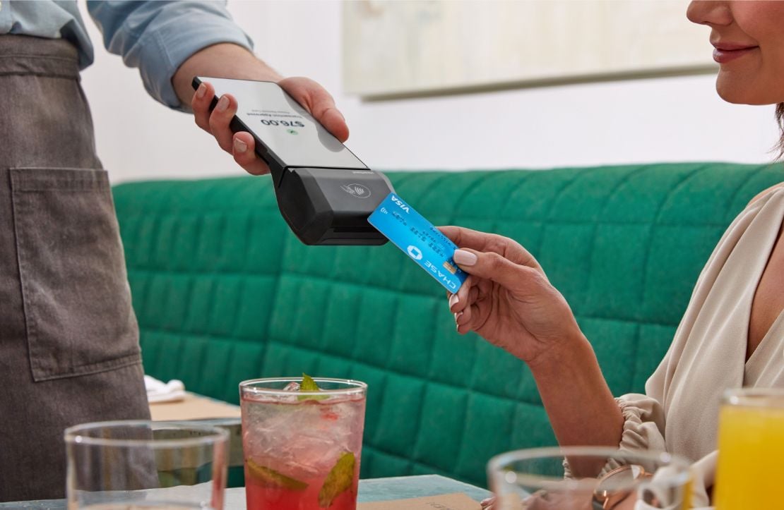 Customer sitting at a restaurant booth tapping credit card on handheld POS held by a waiter