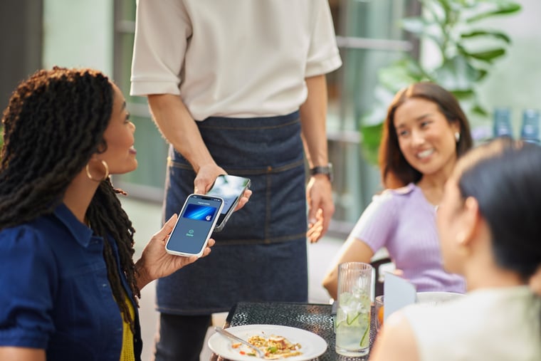 Seated customer using contactless mobile payment to pay server at outdoor restaurant table in patio