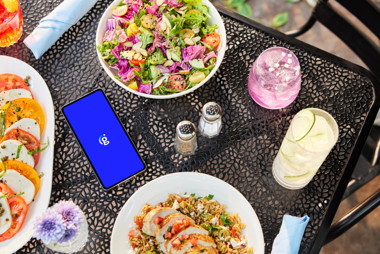 Smartphone displaying bright blue app screen among outdoor dining setup on black metal table