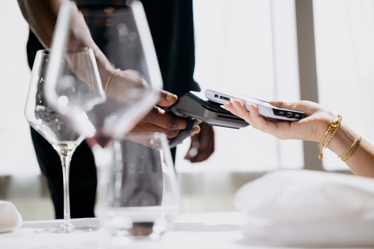 Close-up of seated customer making contactless mobile payment with smartphone at restaurant table