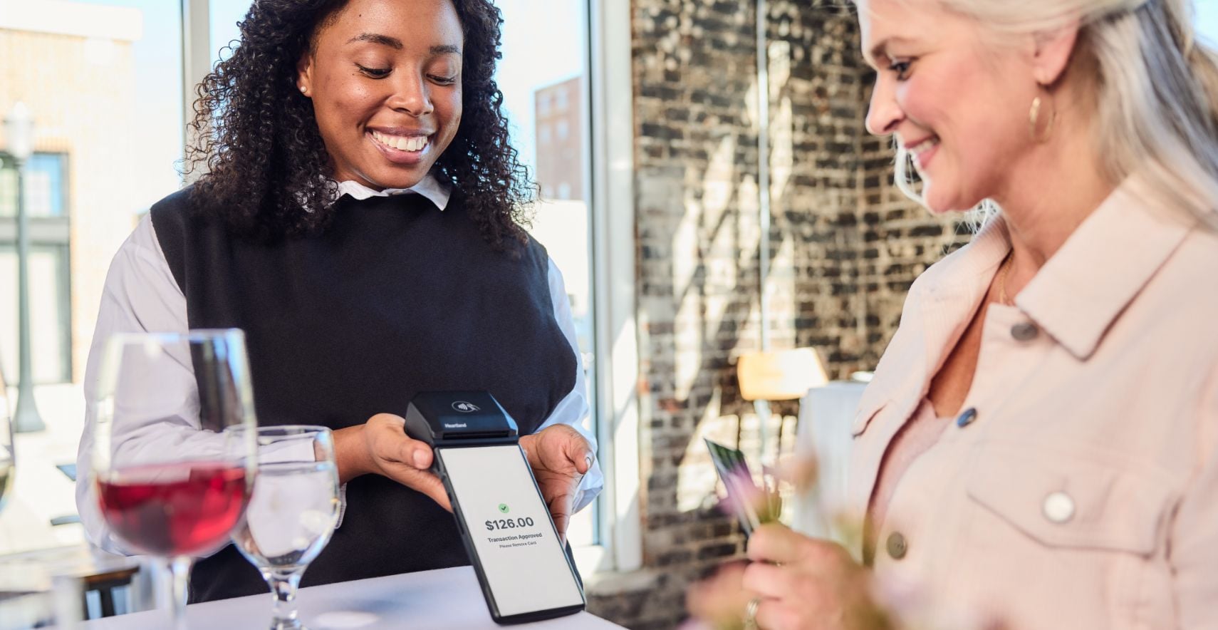 Customer paying for glass of wine on mobile POS device held by server