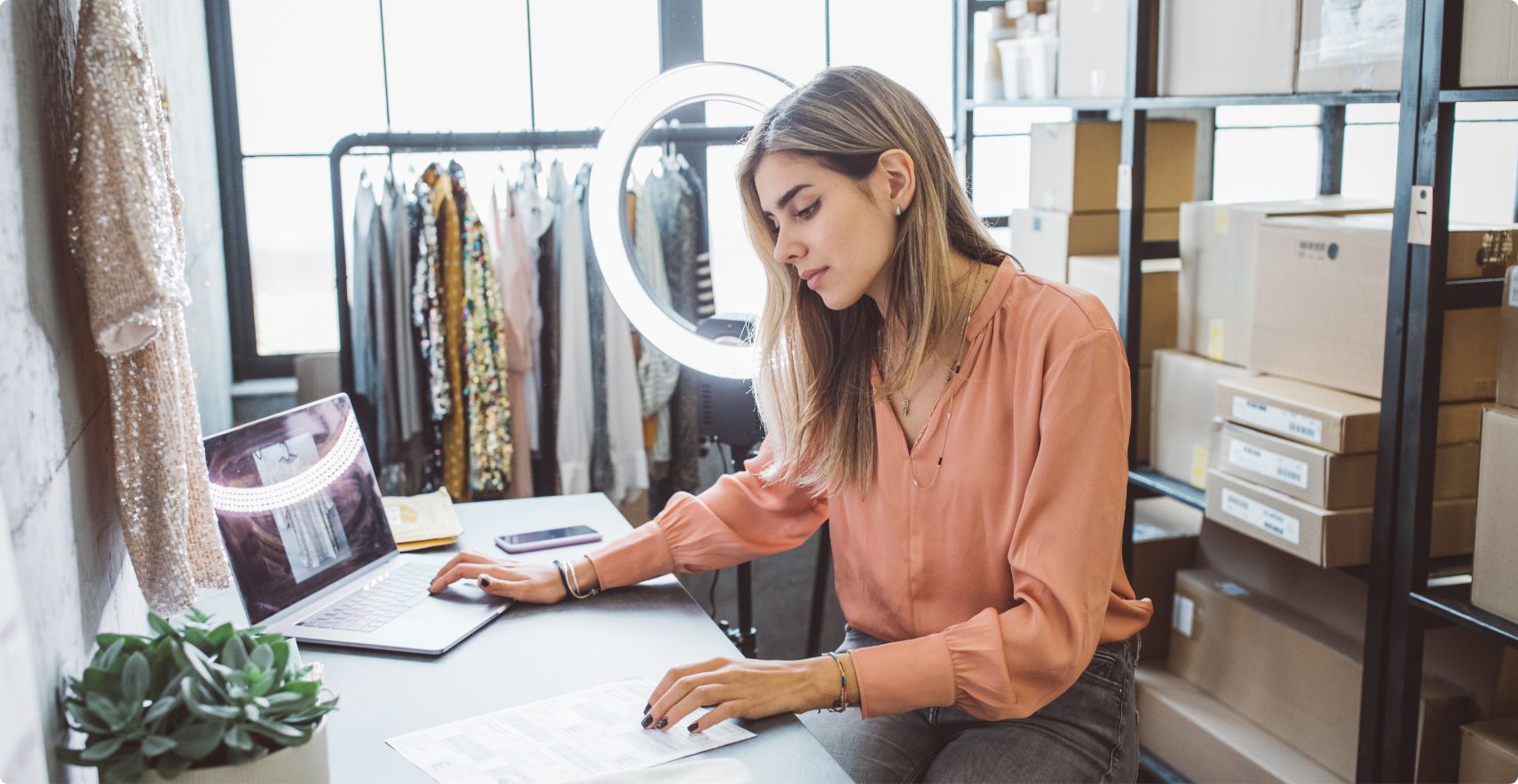 Seated small-business owner, surrounded by merchandise, works on a laptop