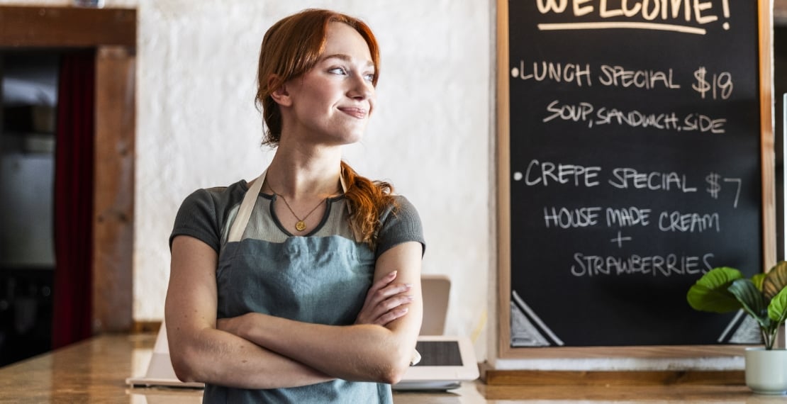 Woman wearing apron works in a cafe while looking hopeful.