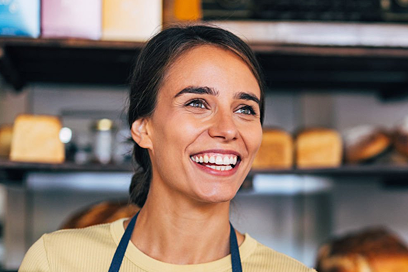 A smiling cafe owner standing behind the counter with shelves of products in the background. 