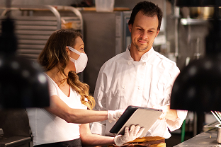 Two restaurant employees looking at tablet in commercial kitchen