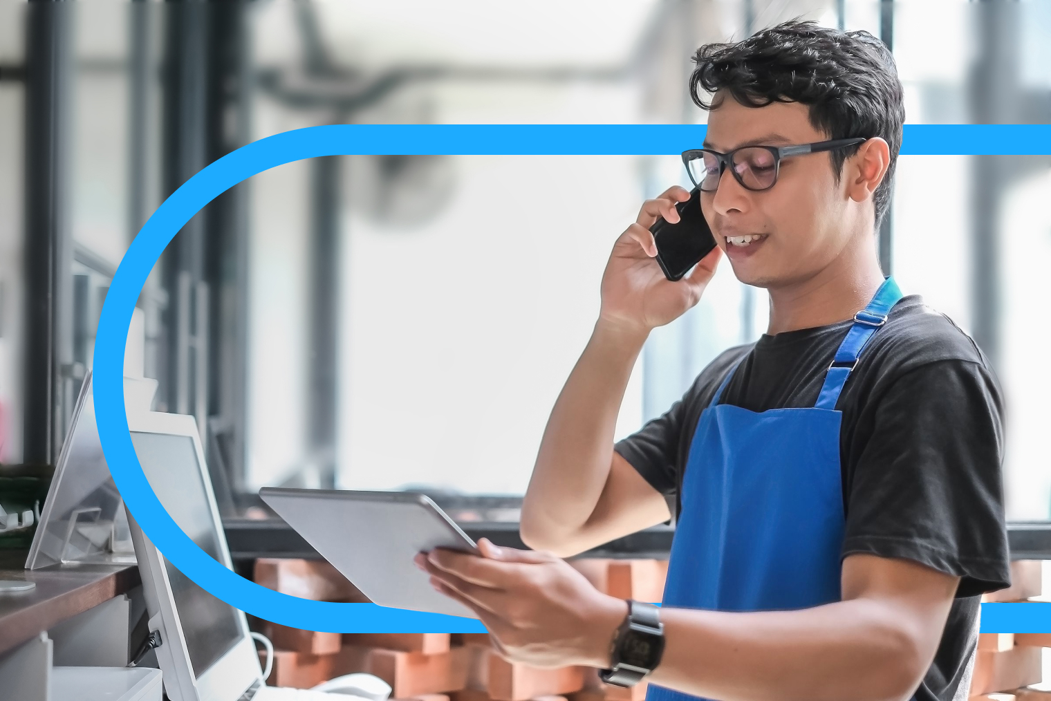 Person wearing apron talks on mobile phone while looking at handheld tablet