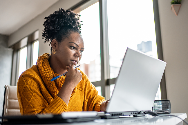 A woman sits in front of an open laptop at a desk.