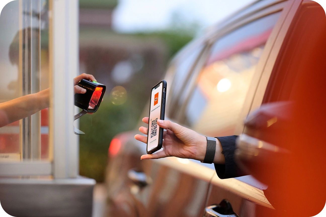 A customer in a drive thru holds out their phone for the service employee to scan.