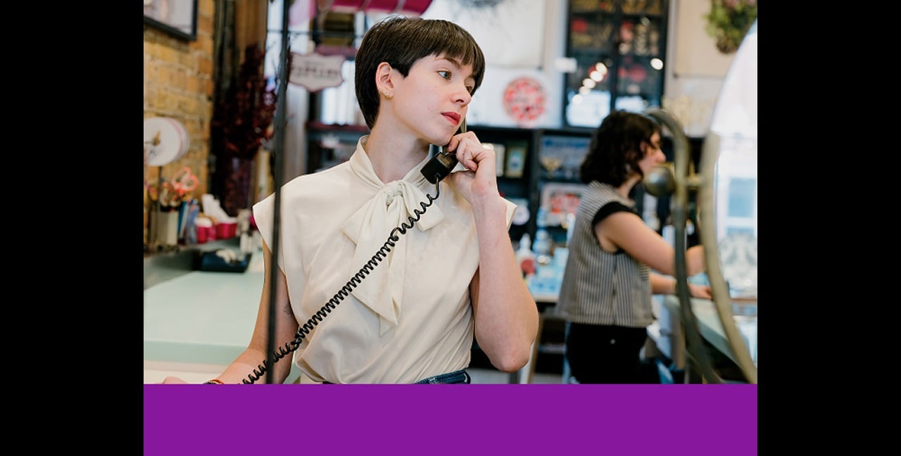 Retail worker talking on a landline behind a checkout counter.