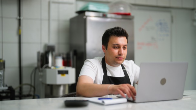 Chef and restaurant owner looks at laptop at the counter in the kitchen of a restaurant