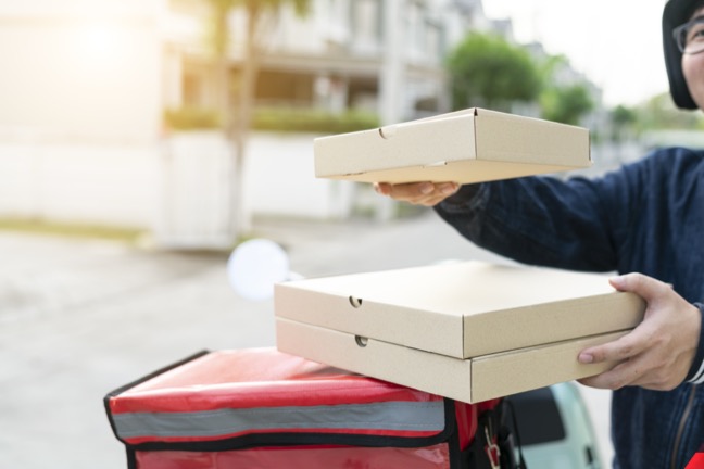 Food delivery driver stacks pizza boxes on back of moped