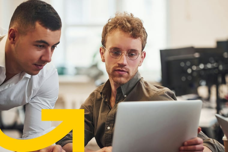 Two colleagues collaborating at office desk while looking at laptop screen