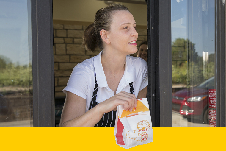Employee of quick-service restaurant handing order through drive-thru window
