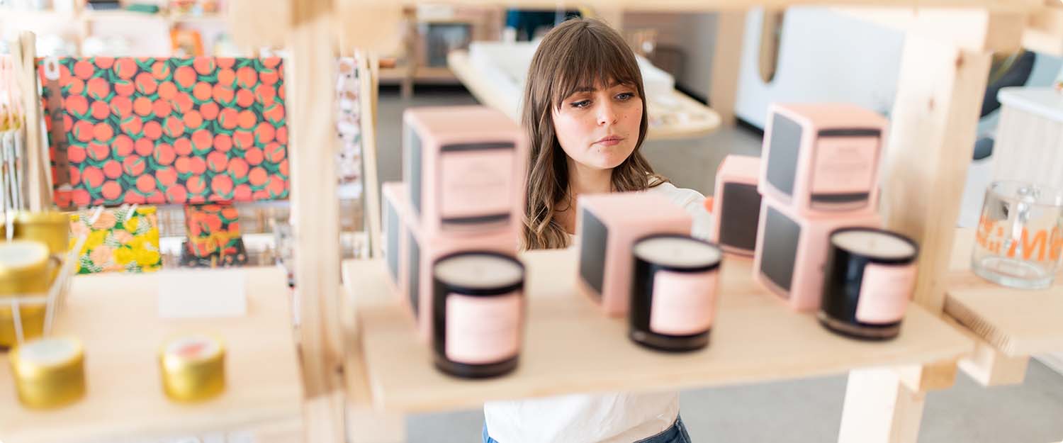 Customer perusing scented candles in jars and boxes displayed on retail shelf