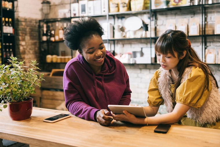 Two small business employees collaborating over tablet behind counter in retail shop