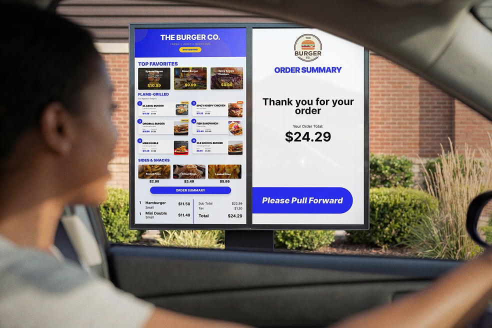 Customer in driver’s seat of car stopping in front of digital menu board at QSR