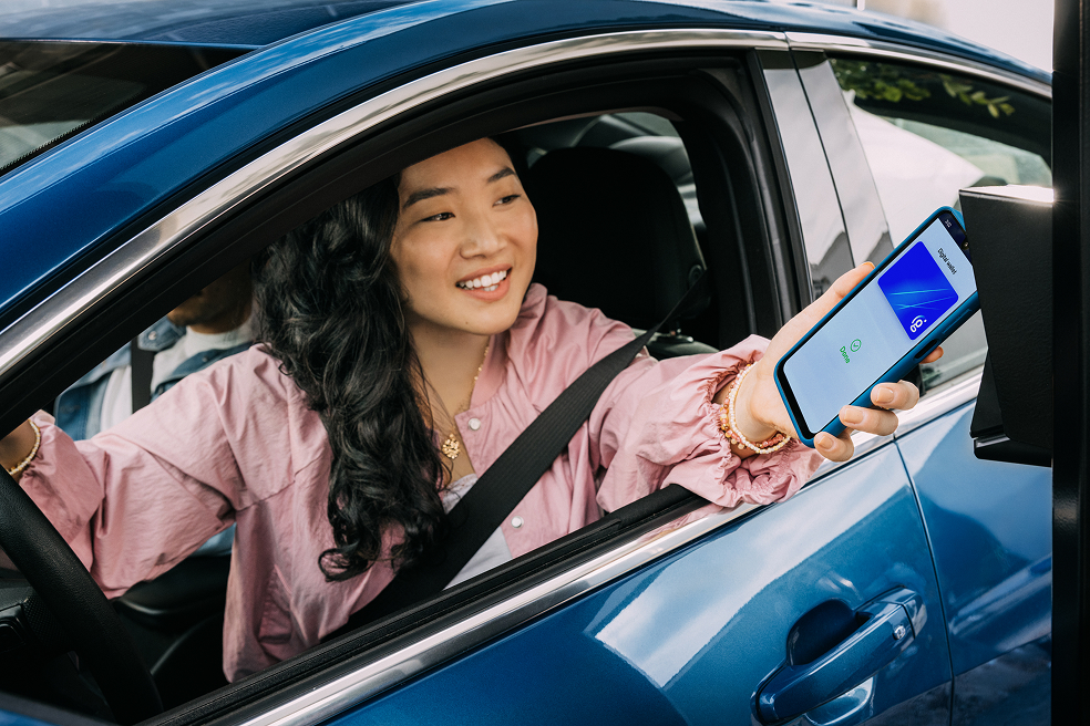 Driver in car holding out smartphone to make contactless payment at drive-thru window of QSR
