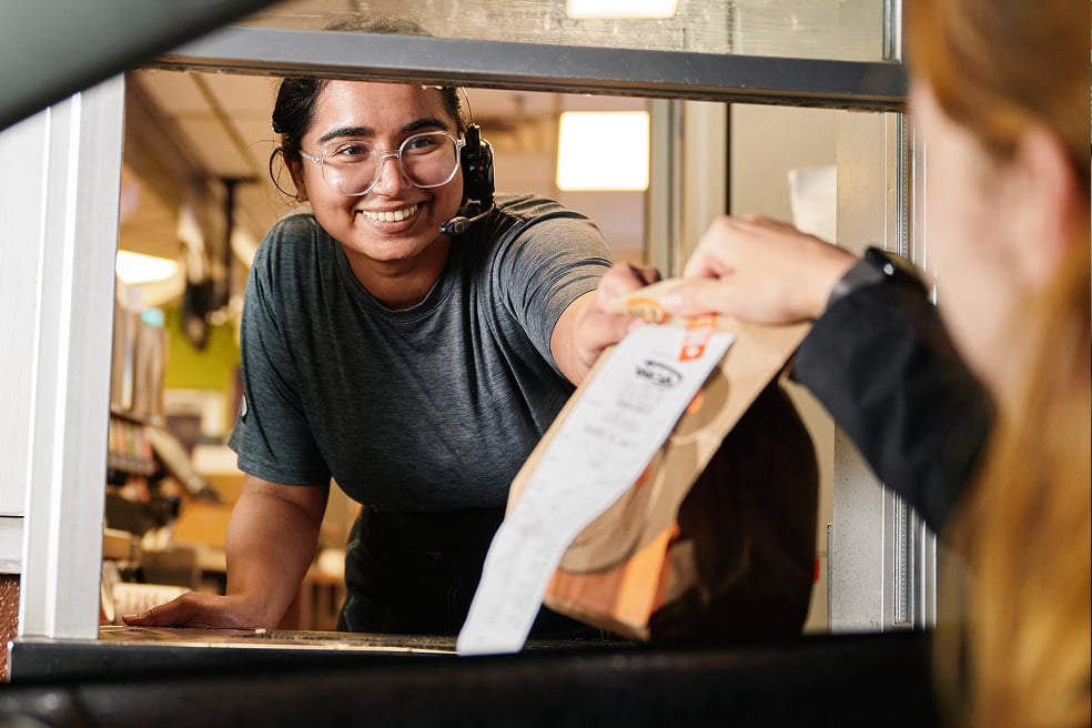 Employee of QSR handing customer bagged food order through drive-thru window