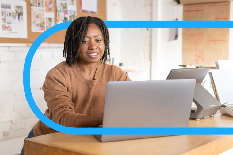 Professional person sits at desk in office and smiles while using laptop