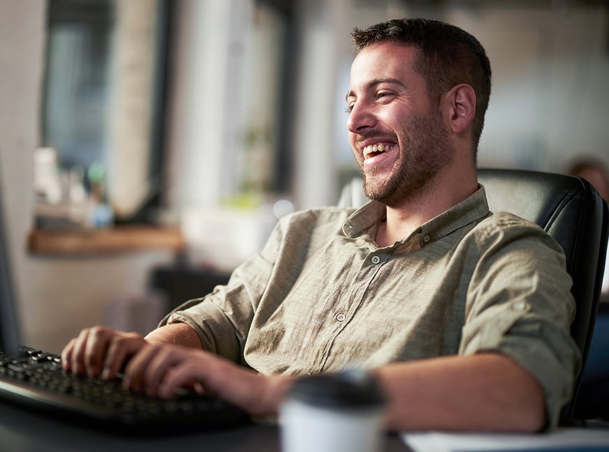Developer typing on a computer sits in his office and smiles.