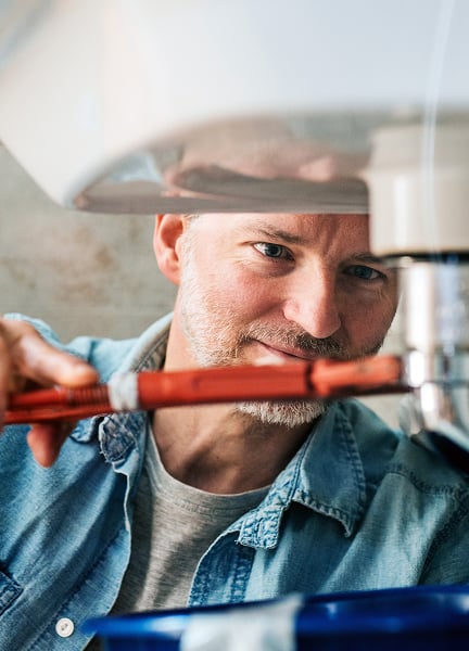 Home services worker uses a wrench to fix a pipe beneath a customer’s sink.