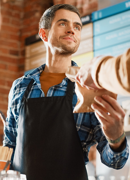 Cafè worker hands a customer food in a brown paper bag.