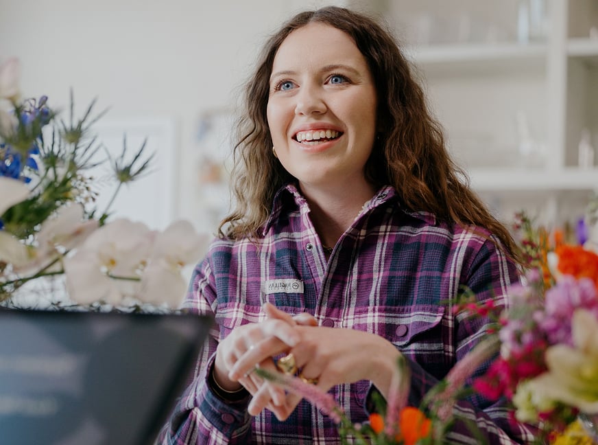 Person wearing a plaid shirt smiles in a flower shop.