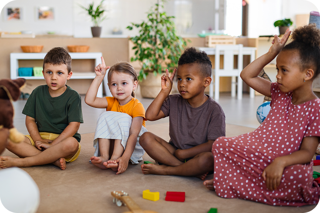 A group of children sit in a circle in a childcare centre while playing a game.