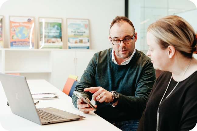 Two people sit at a desk in front of a laptop and discuss payment integrations.