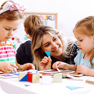 A childcare worker plays with two children at a table.