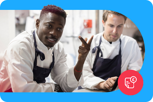 Two restaurant staff wearing black aprons work in a commercial kitchen.