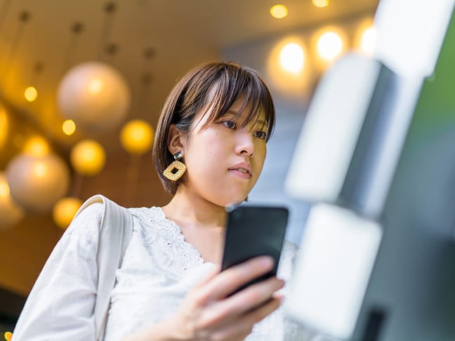 Une femme tenant un smartphone tout en utilisant une borne ou une machine en libre-service.
