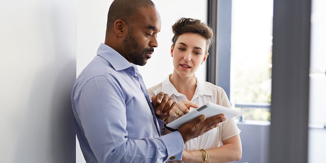 Man and woman in professional attire looking at a digital tablet together.