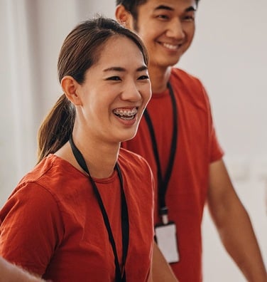 Two smiling nonprofit workers in orange scrubs with badges