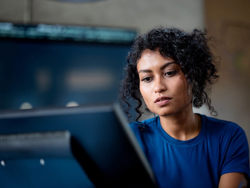 Femme concentrée aux cheveux bouclés regardant attentivement un écran d'ordinateur.