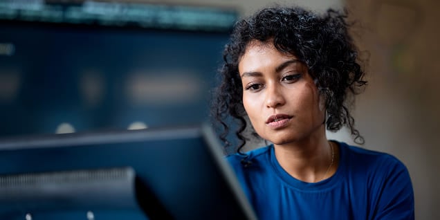 Woman wearing a blue top attentively working at her desk computer.