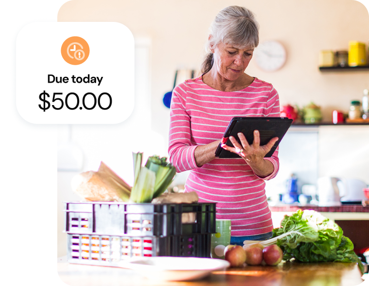 A senior woman manages her budget on a tablet next to a basket of fresh kitchen produce.